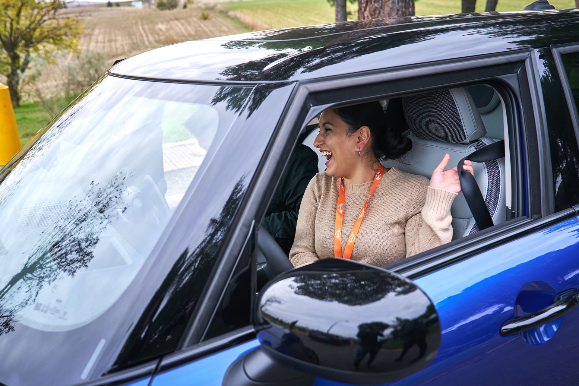 A joyful woman sits in the driver’s seat of a blue MINI, laughing with excitement.